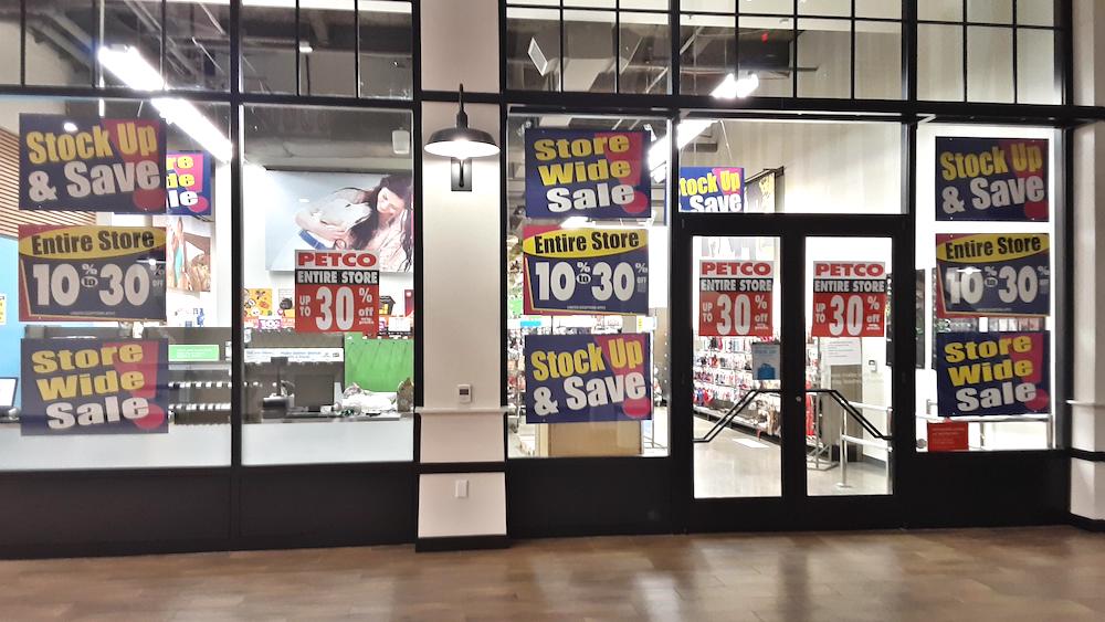 Storefront with large signs reading “Stock Up & Save” and “Entire Store 10%-30% Off,” indicating a sale at Petco. The store interior and product shelves are visible through the windows.