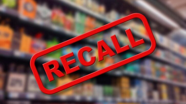A blurred supermarket shelf with various products, overlaid by a large red "RECALL" stamp in the center of the image.