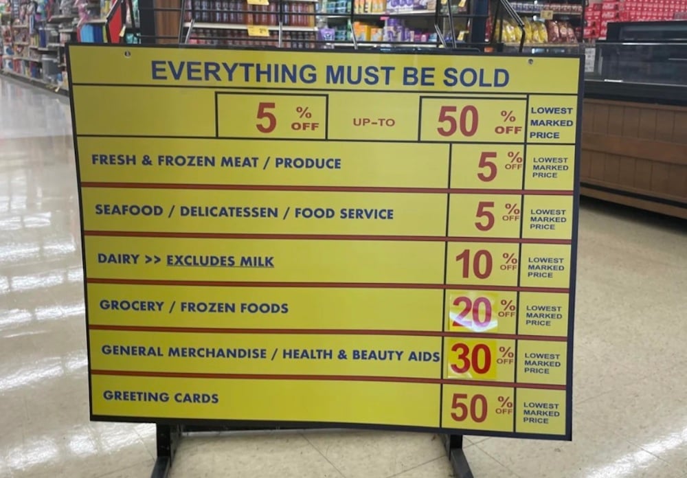 A large yellow sign in a Safeway grocery store displays discounts of 5% to 50% off various items, including fresh food, seafood, dairy, groceries, merchandise, and greeting cards. The sign reads, "Everything must be sold.
