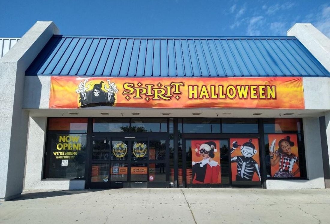 Storefront of Spirit Halloween with a bright orange sign, images of children in costumes on the windows, and a “Now Open” and “We’re Hiring” sign by the entrance—stay tuned for Spirit Christmas 2025 locations coming soon!