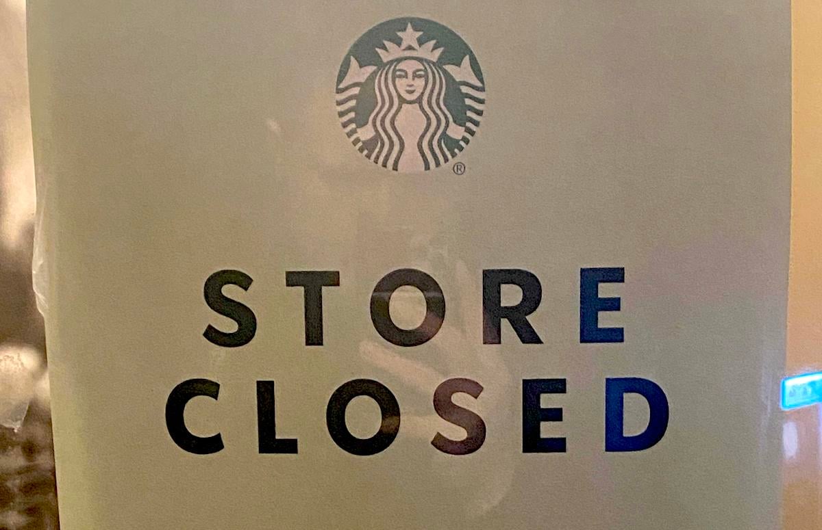 A sign with the Starbucks logo at the top reads "STORE CLOSED" in bold, black letters. The sign appears to be posted on a glass door or window.