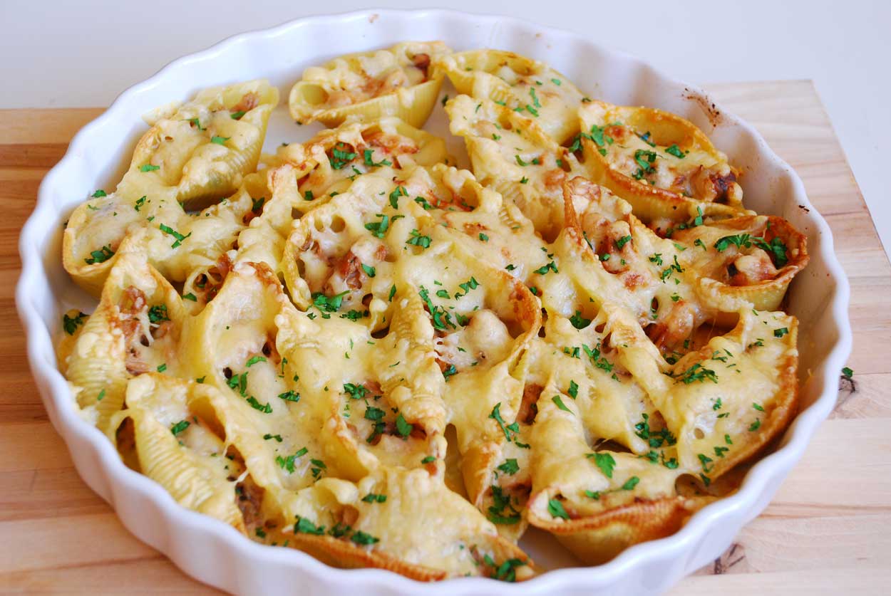 A round white baking dish filled with large pasta shells stuffed with filling, topped with melted cheese and sprinkled with chopped parsley, bringing a taste of classic diner foods to your table on a wooden surface.
