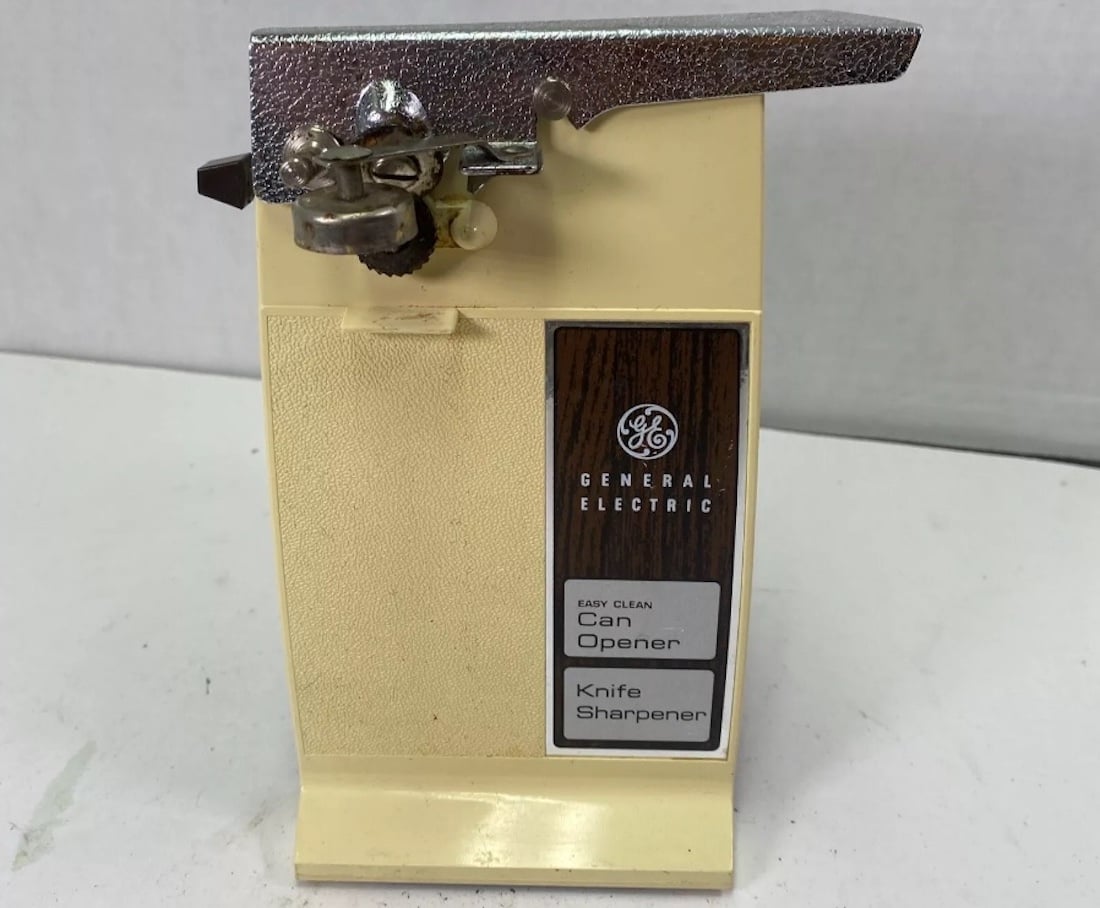 A vintage cream and silver General Electric electric can opener with a built-in knife sharpener and wood-patterned accent, displayed on a white surface.