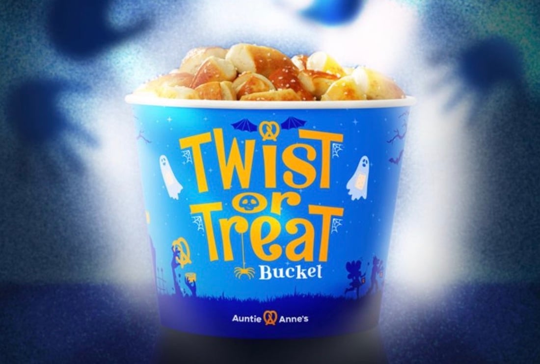 A blue Auntie Anne’s bucket filled with pretzel bites features Halloween-themed designs, including ghosts, bats, and the words “Twist or Treat Bucket” in bold yellow letters.