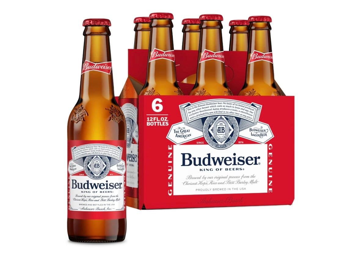 A six-pack of Budweiser beer in 12 fl oz glass bottles, with one bottle in front and the rest in a red cardboard carrier featuring the Budweiser logo and branding.