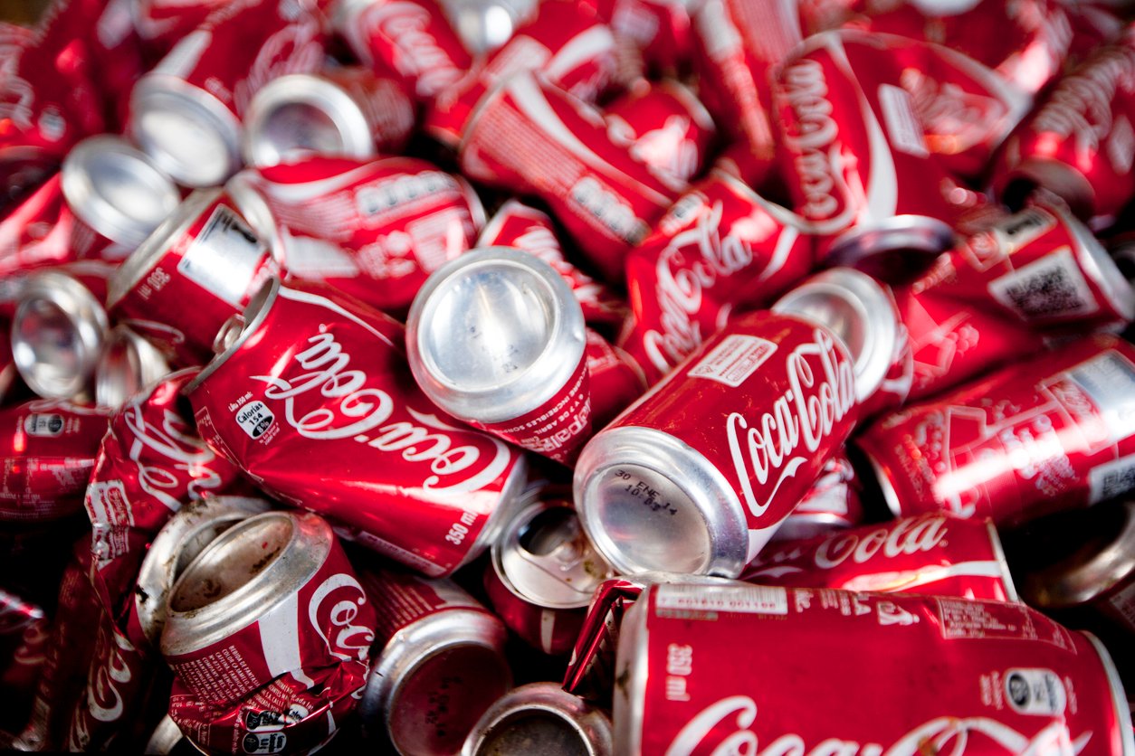 A large pile of empty, crushed red Coca-Cola cans, some stacked and some scattered, with labels and logos visible.
