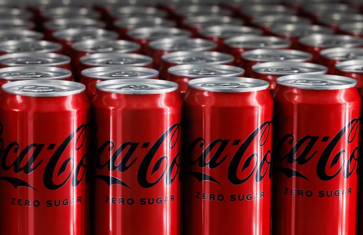 Rows of red Coca-Cola Zero Sugar cans are lined up closely together, showing the tops and part of the logos in a repeating pattern.