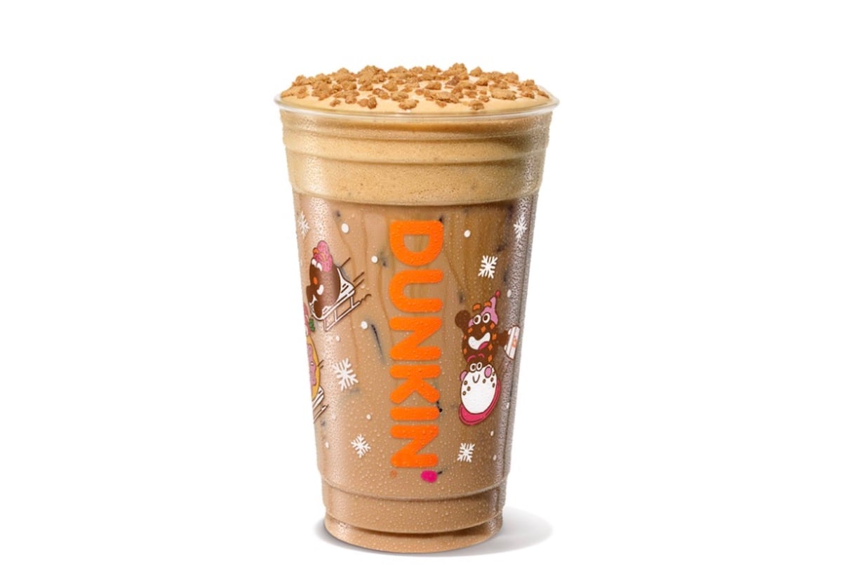 A Dunkin’ holiday-themed cup filled with a blended iced coffee drink, topped with a layer of foam and sprinkled crumbles, featuring festive winter graphics and the orange Dunkin’ logo.