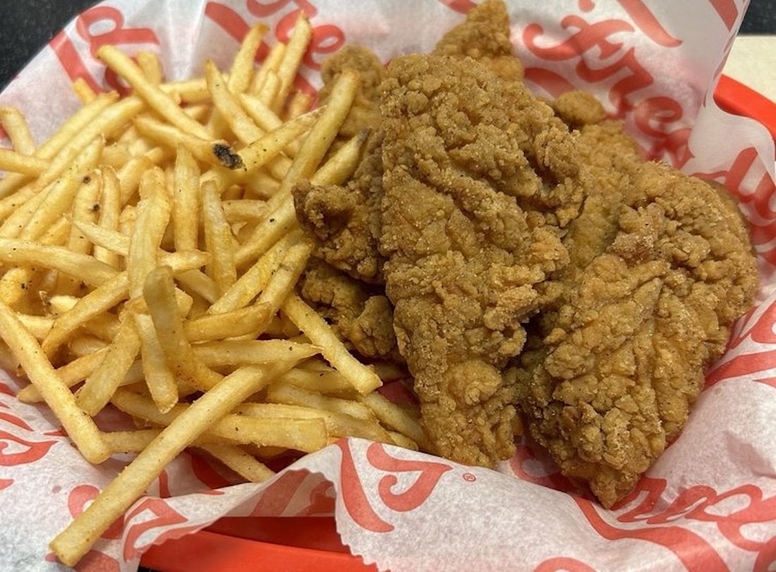 A basket lined with branded paper holds crispy golden French fries and several pieces of breaded fried chicken tenders.