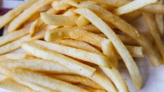 A close-up view of several golden, crispy French fries arranged in a pile on a white surface.