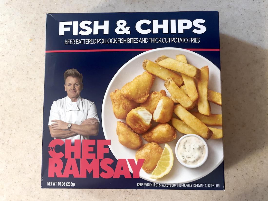 A box of Chef Ramsay Fish & Chips, featuring beer-battered pollock fish bites, thick-cut fries, a lemon wedge, tartar sauce, and a photo of Gordon Ramsay with his arms crossed on the packaging.