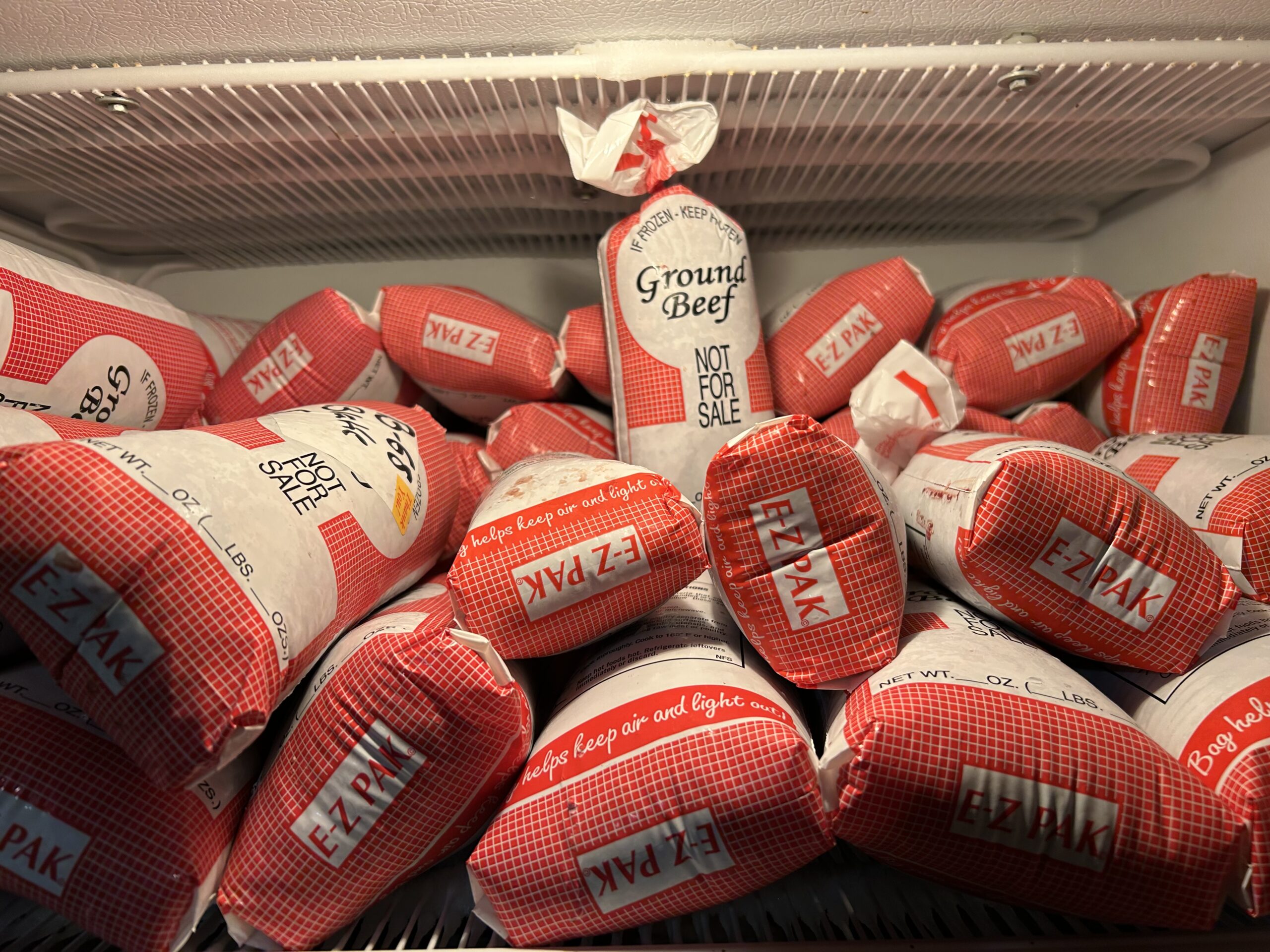Several packages of ground beef labeled "EZ Pak" are stacked inside a freezer. One package in the back is labeled "Ground Beef Not for Sale." Frost lines are visible on the freezer shelf above.