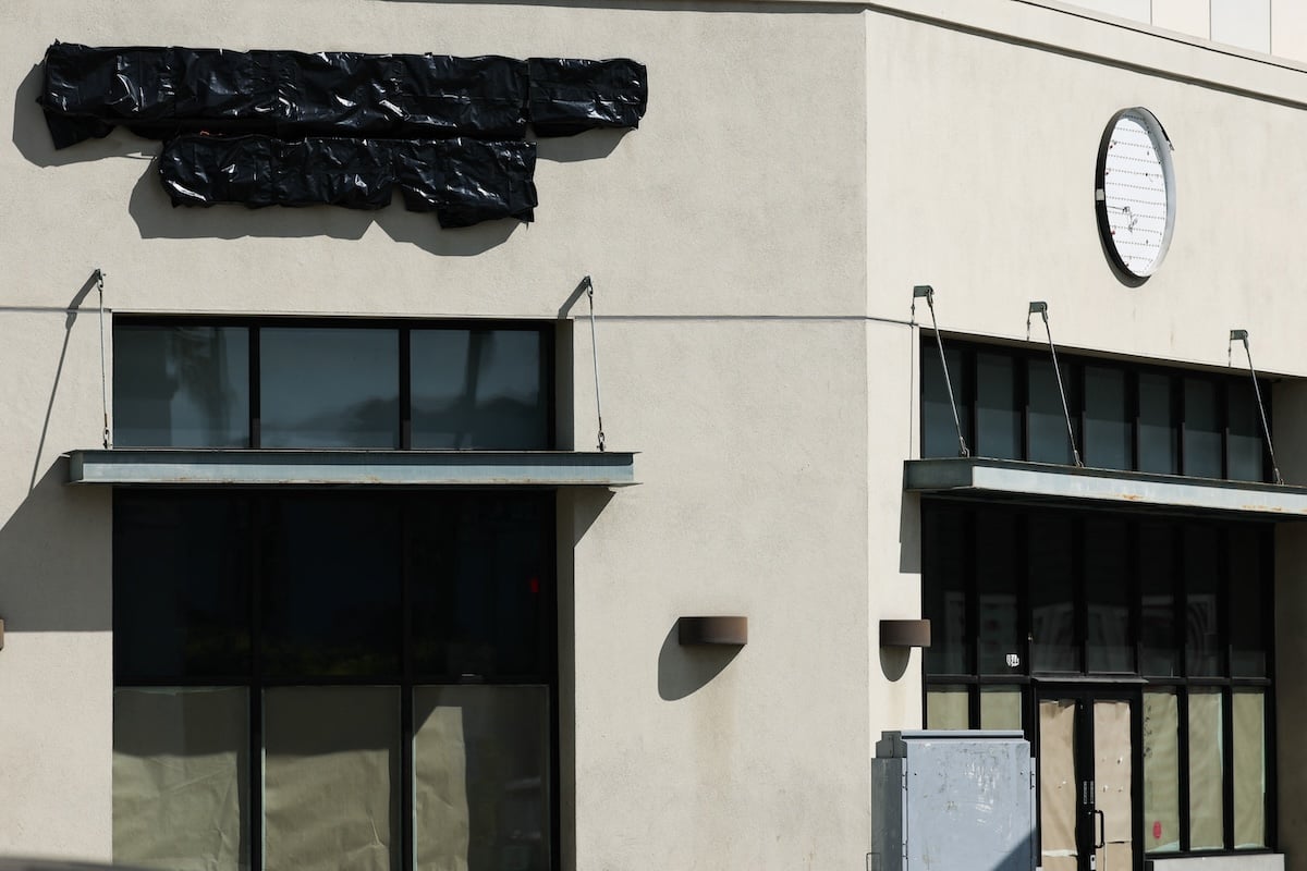A closed storefront with covered windows, a sign wrapped in black plastic, and a blank circular sign on the beige exterior wall, indicating the business is no longer operating.