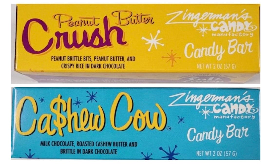 Two candy bars from Zingerman's Candy Manufactory: "Peanut Butter Crush" in a yellow box and "Ca$hew Cow" in a blue box, both featuring playful fonts and decorative star accents.