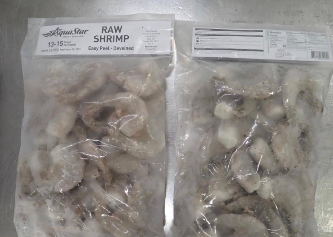 Two clear plastic bags of frozen, raw, deveined shrimp labeled "Aqua Star RAW SHRIMP" on a metal surface. The shrimp in both bags are visibly frosty and packed tightly together.