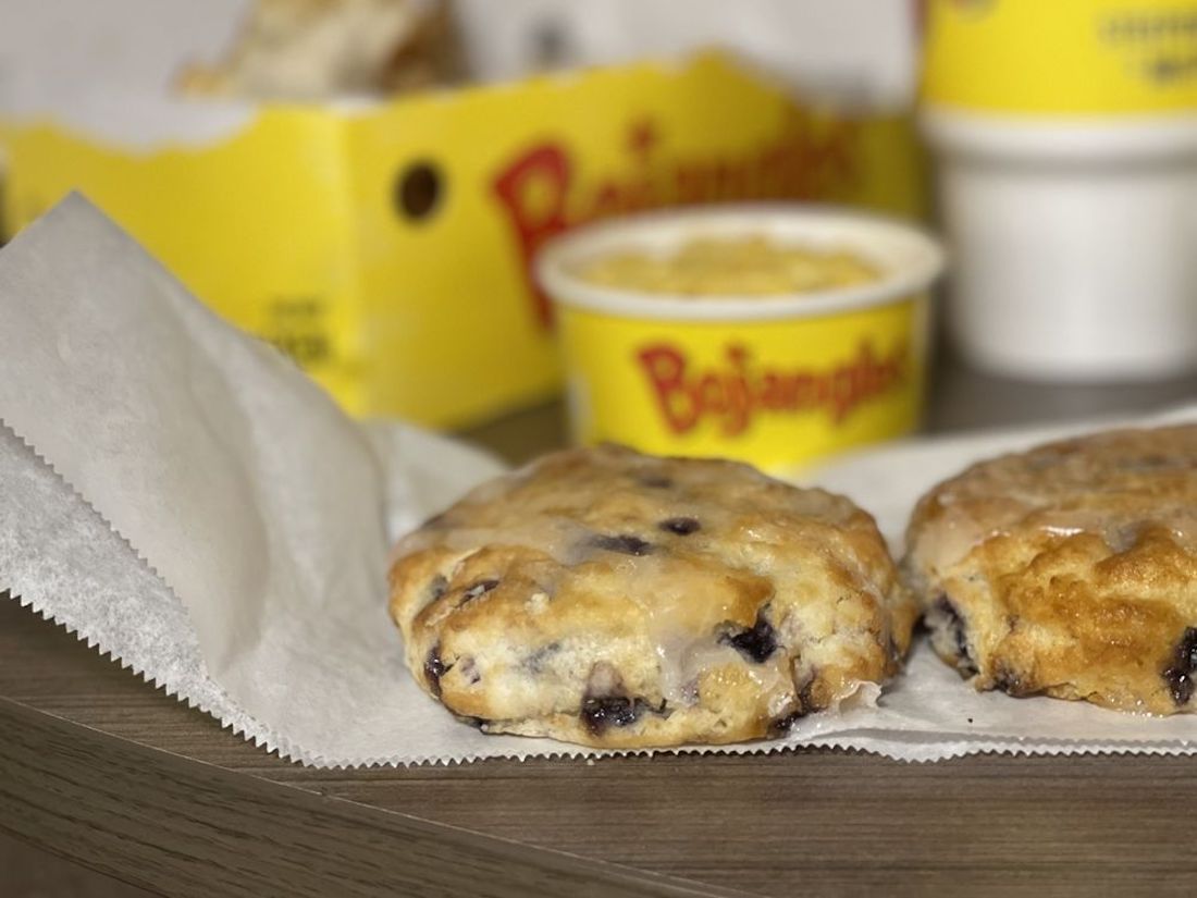 A close-up of two glazed blueberry biscuits on parchment paper, with a cup of yellow Bojangles’ branded food and a yellow box blurred in the background.
