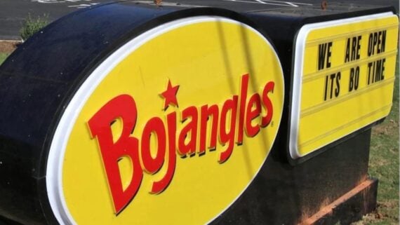 A Bojangles restaurant sign with a yellow oval logo and red text. Next to it, a message board reads, "WE ARE OPEN ITS BO TIME" in black letters on a yellow background.