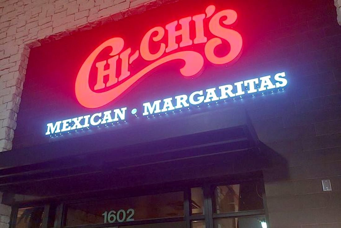 A brightly lit restaurant sign reads "Chi-Chi’s" in red cursive letters above "Mexican • Margaritas" in white lettering, mounted on a stone and brick exterior wall.