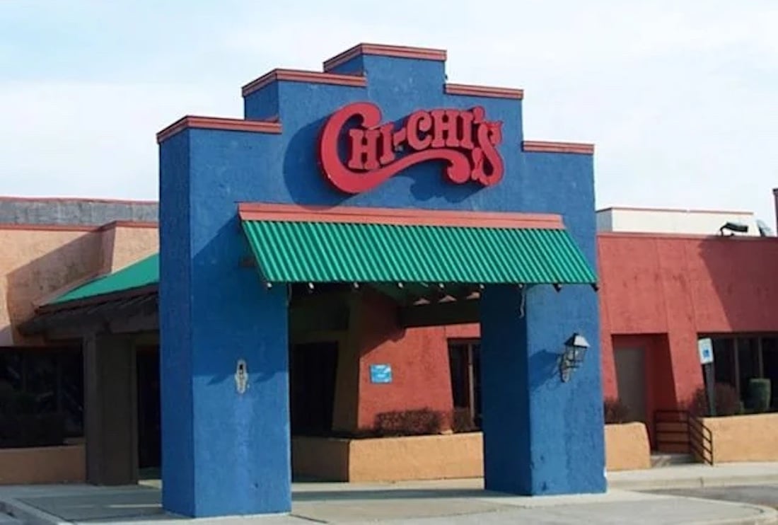 A restaurant entrance with a blue facade and green awning, featuring a red sign that reads "Chi-Chi's" in stylized letters. The building has orange and tan walls in the background.