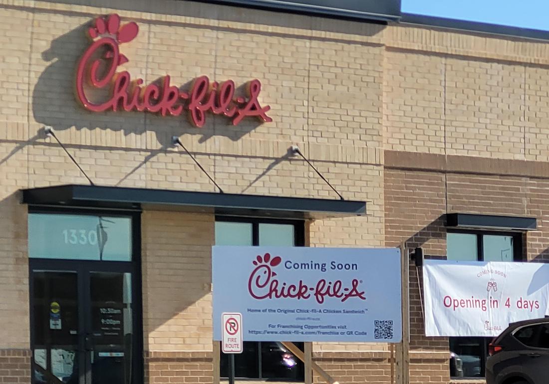 A Chick-fil-A restaurant with a “Coming Soon” sign outside and a banner that reads “Opening in 4 days” displayed on the brick exterior of the building.