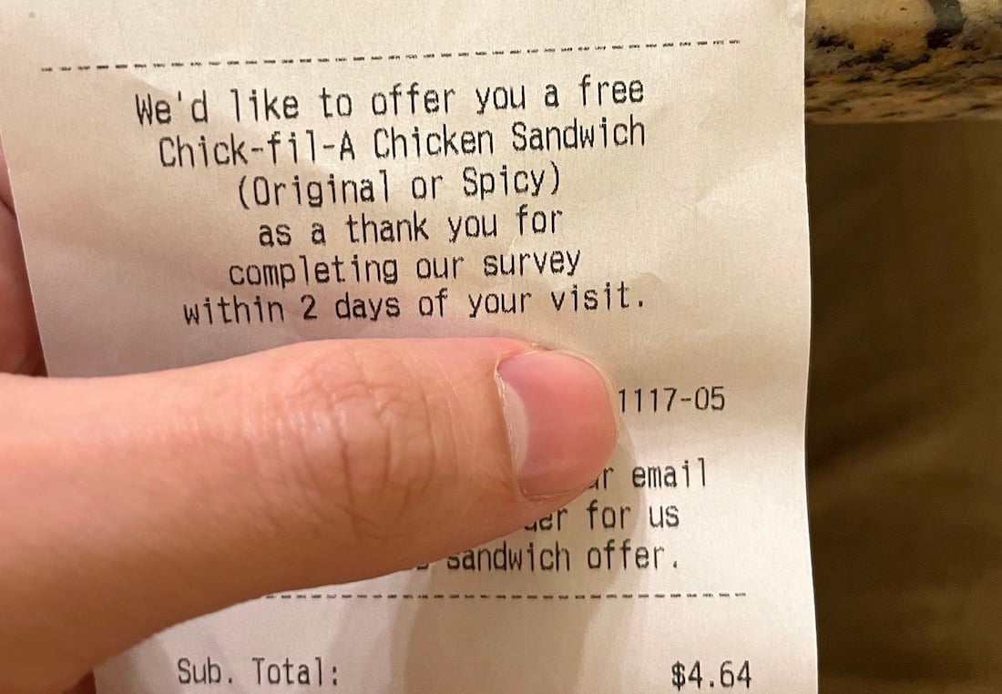 A hand holding a Chick-fil-A receipt offering a free chicken sandwich for completing a survey within two days of the visit. The receipt total is $4.64.