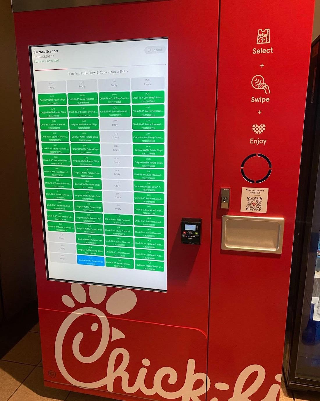 A red Chick-fil-A self-service kiosk with a large touchscreen displaying a grid of food item statuses, a card reader, receipt slot, and instructions to select, swipe, and enjoy.