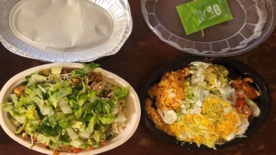 Two takeout bowls filled with Mexican food—one with lettuce, rice, beans, and cheese, and the other with rice, shredded cheese, lettuce, and guacamole. Also shown are a covered dish and a packet of green hot sauce.