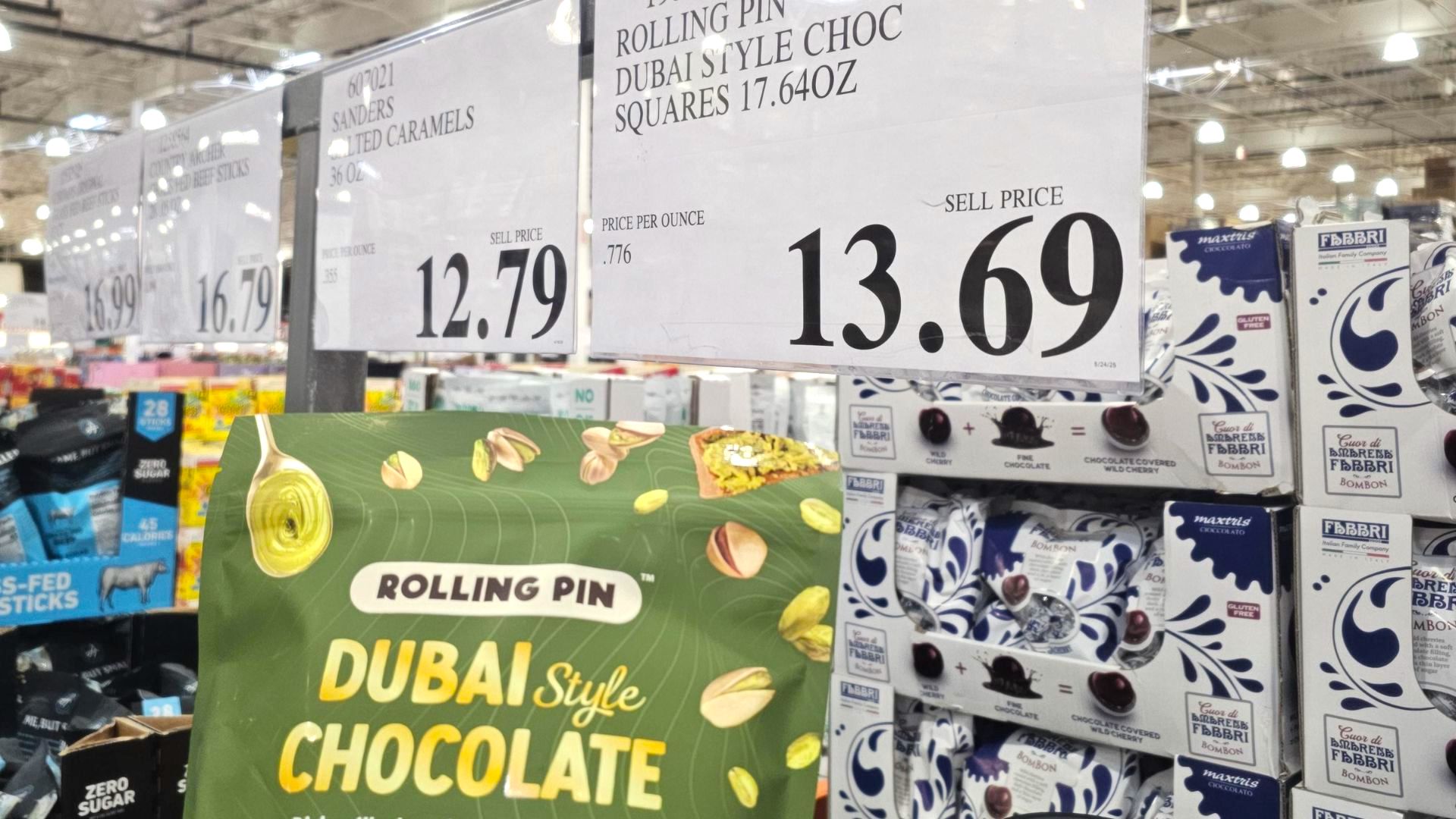 A close-up of a grocery store shelf shows a "Rolling Pin Dubai Style Chocolate" package and a price sign above it displaying $13.69. Other food products and price tags are visible in the background.
