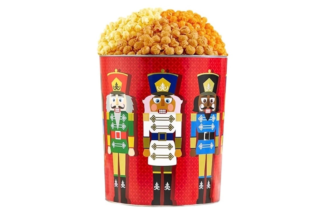 A large popcorn bucket featuring illustrations of three colorful toy soldiers in uniform, set against a red background, filled to the top with golden popcorn.