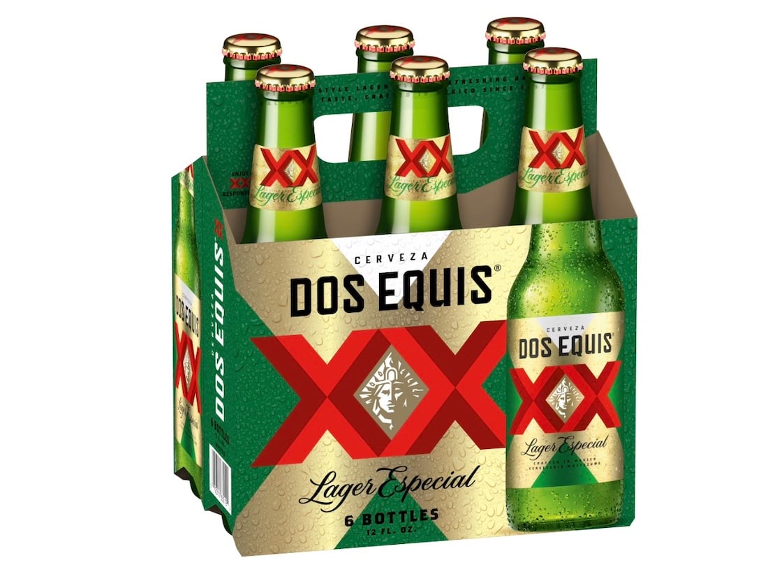 A six-pack of Dos Equis Lager Especial beer bottles in a green and gold cardboard carrier, featuring large red "XX" logos and the brand name prominently displayed on both the bottles and the packaging.