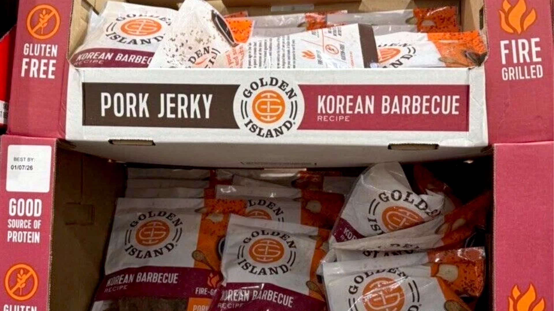 A display box of Golden Island Korean Barbecue Pork Jerky packs, labeled as fire grilled, gluten free, and a good source of protein. The packaging is red and white with visible jerky inside the bags.