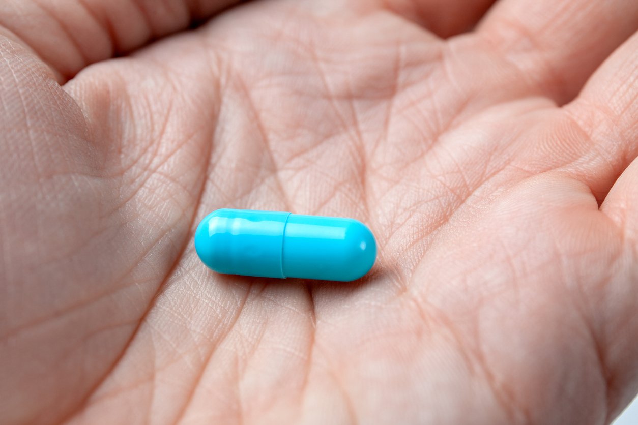A close-up of a person's hand holding a single bright blue capsule-shaped pill in their palm.