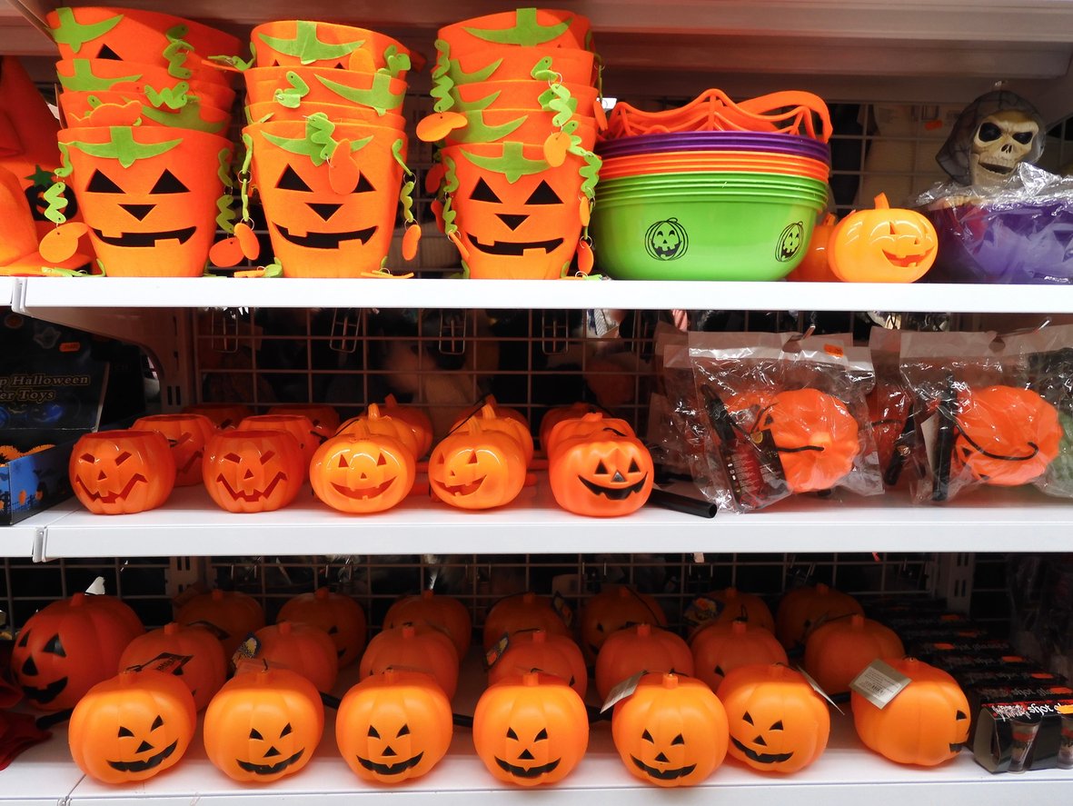 Shelves filled with various plastic Halloween pumpkin buckets and decorations, mostly orange with jack-o’-lantern faces, and a few green buckets, set up for Halloween.