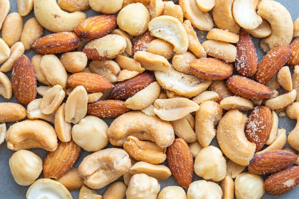 A close-up of a mixed variety of salted nuts, including almonds, cashews, hazelnuts, and peanuts, showing their textures and colors.