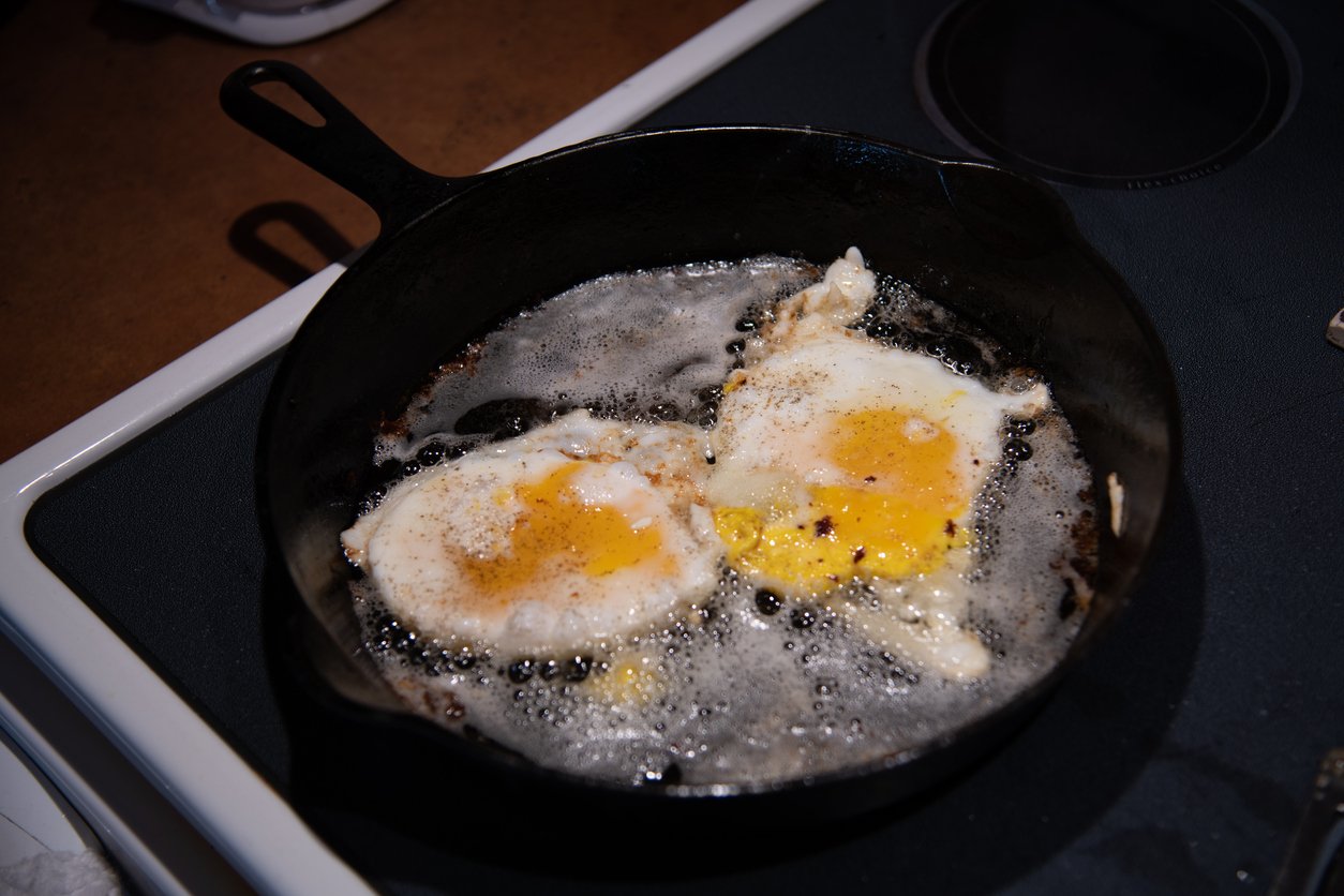 Two sunny-side-up eggs frying in a cast iron skillet with bubbling oil, sitting on a stovetop.