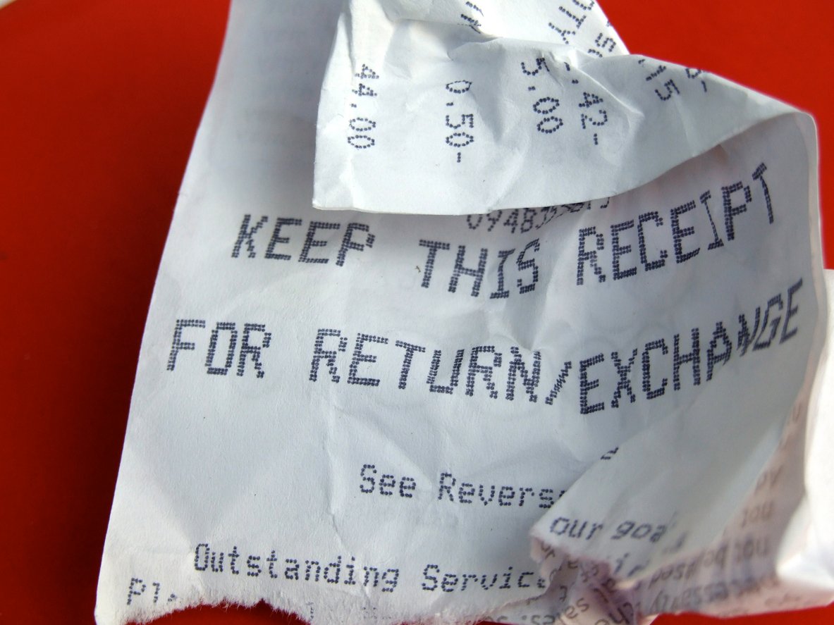 A crumpled paper receipt with the text "KEEP THIS RECEIPT FOR RETURN/EXCHANGE" printed on it, lying on a red surface.