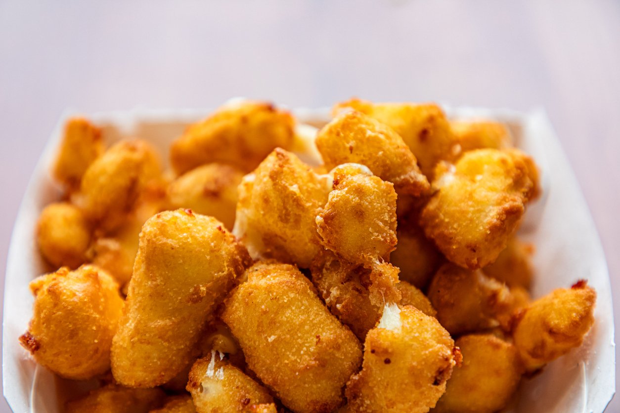 Close-up of a basket filled with golden-brown, crispy fried cheese curds, with a soft, blurred background.