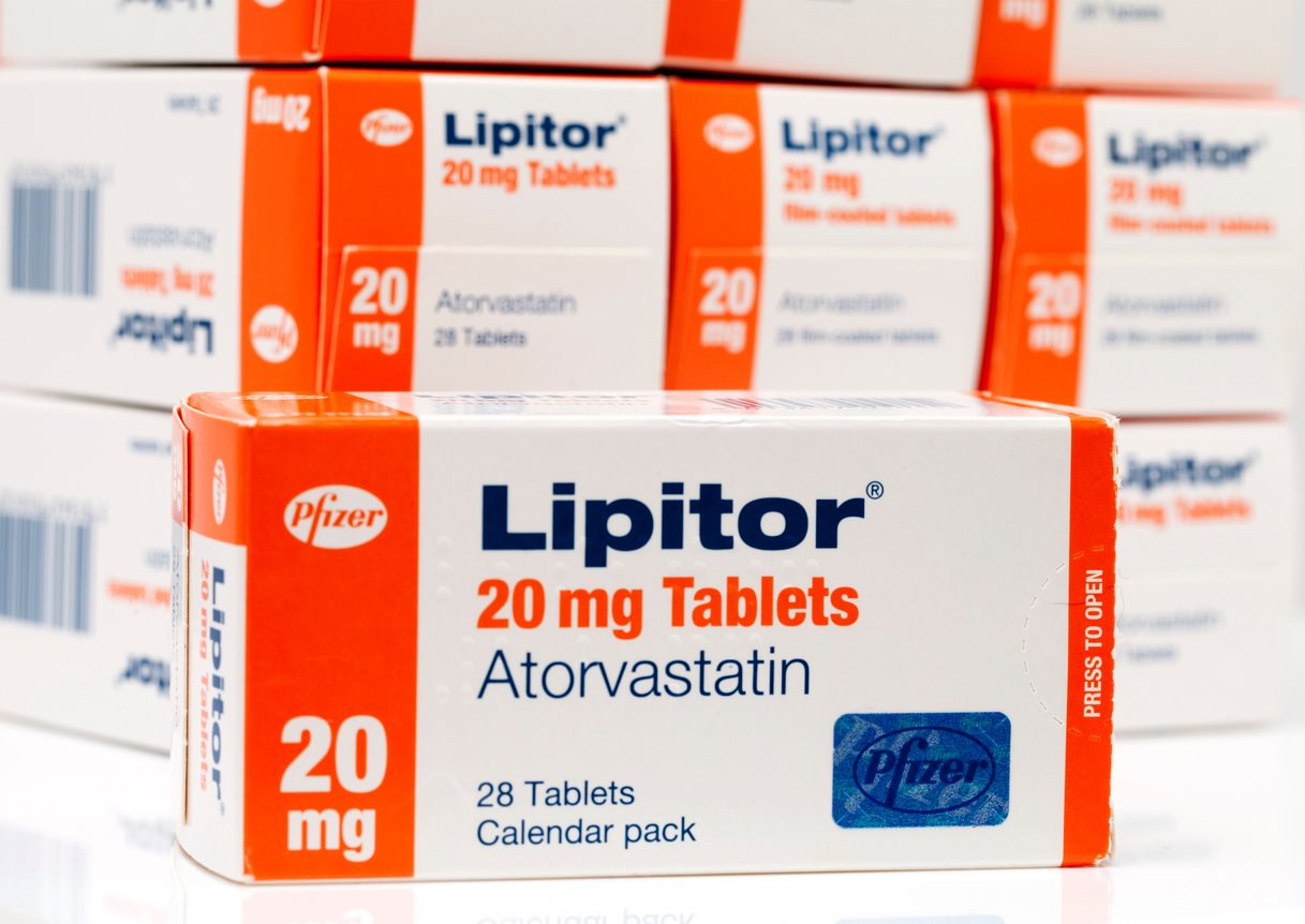 A close-up of a box of Lipitor 20 mg tablets (atorvastatin) by Pfizer, with several similar boxes stacked in the background. The package contains 28 tablets and is labeled as a calendar pack.