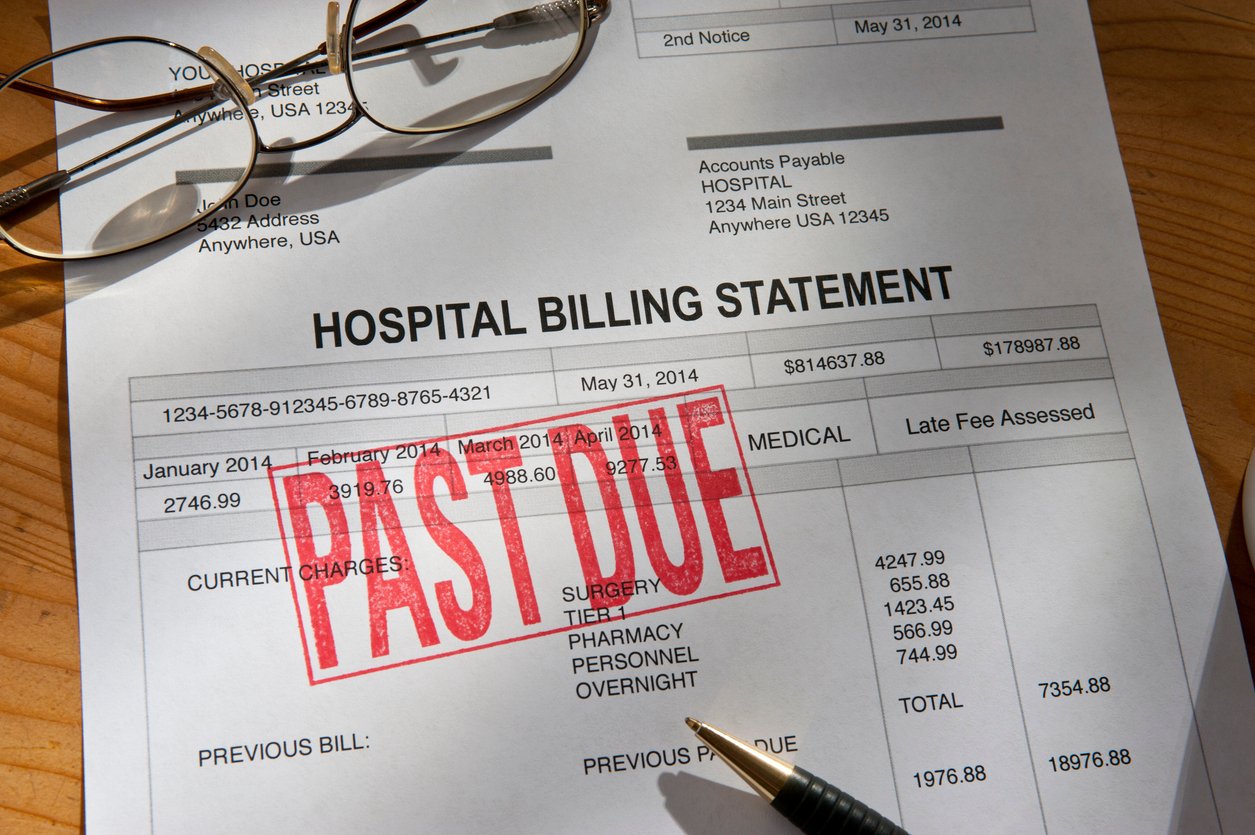 A hospital billing statement with a large red "PAST DUE" stamp across it, glasses, and a pen resting nearby on a wooden desk.