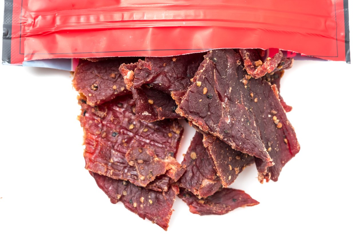 Beef jerky pieces spilling out of a partially opened red resealable bag on a white background.