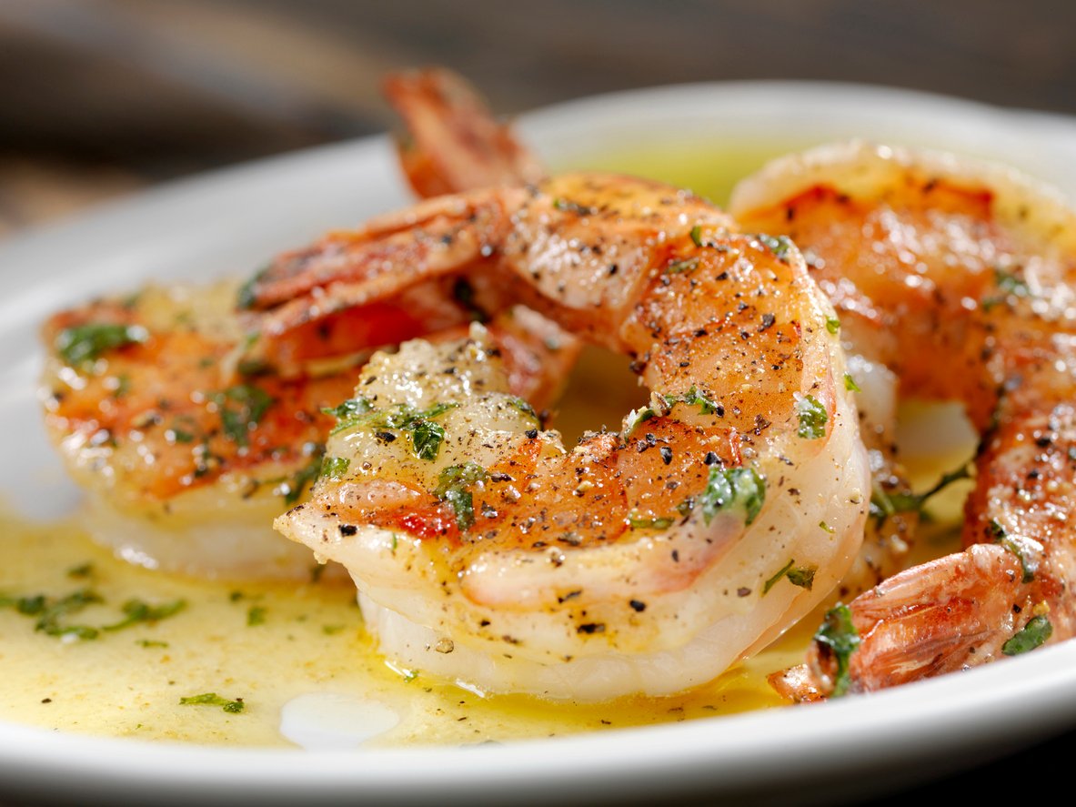 Close-up of cooked shrimp seasoned with herbs and black pepper, served in a buttery sauce on a white plate.