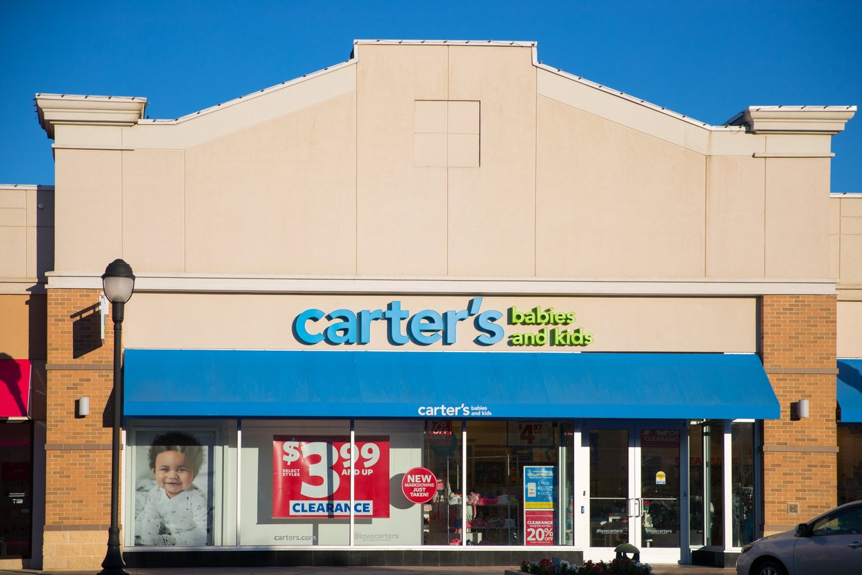 A Carter’s Babies and Kids store with a blue awning, large glass windows, and a sign advertising a clearance sale. A poster with a smiling baby is visible in the front window.