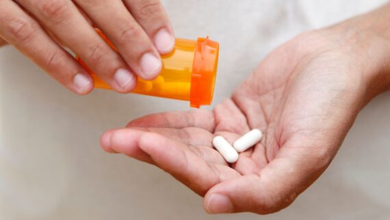 A person pours two white capsules from an orange pill bottle into their hand.
