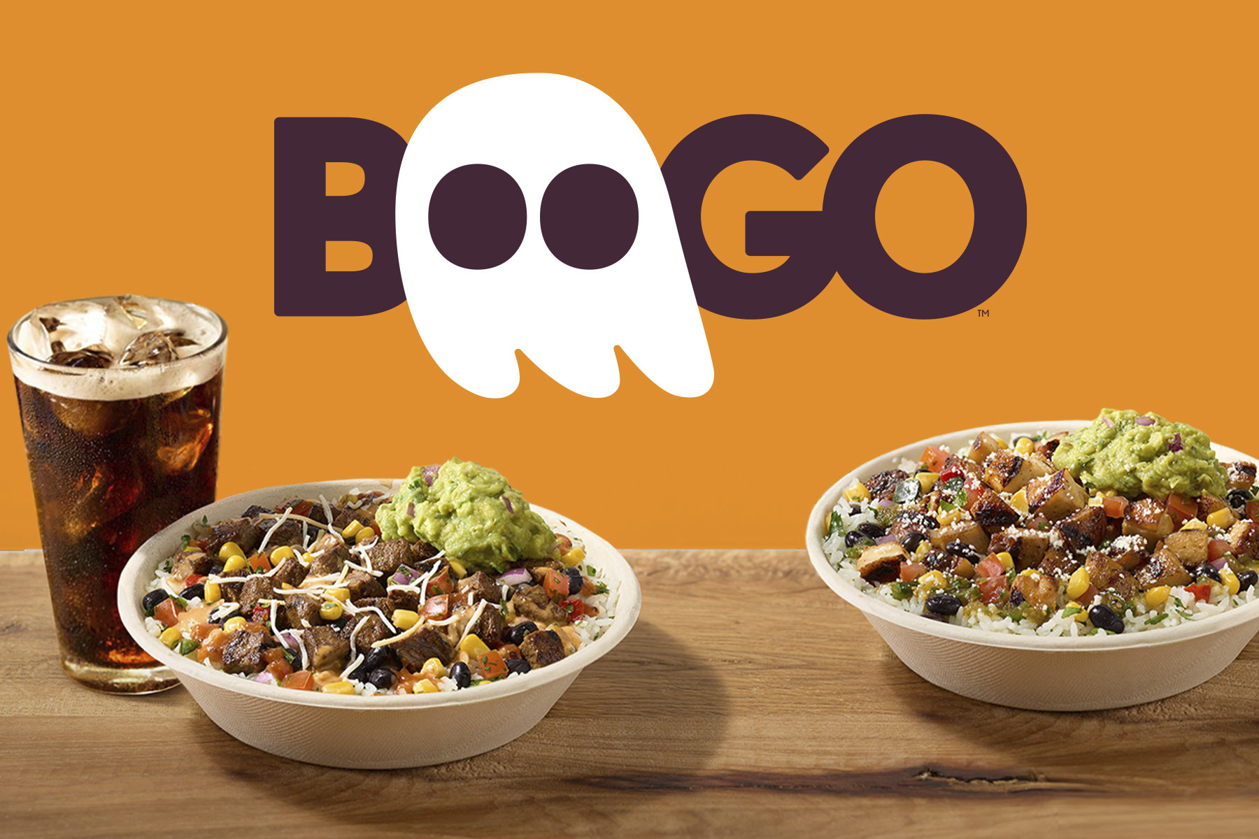 Two burrito bowls and a glass of soda on wooden tables, with the word "BOOGO" in large letters behind them. The "O"s are stylized to resemble ghost eyes. The background is orange.