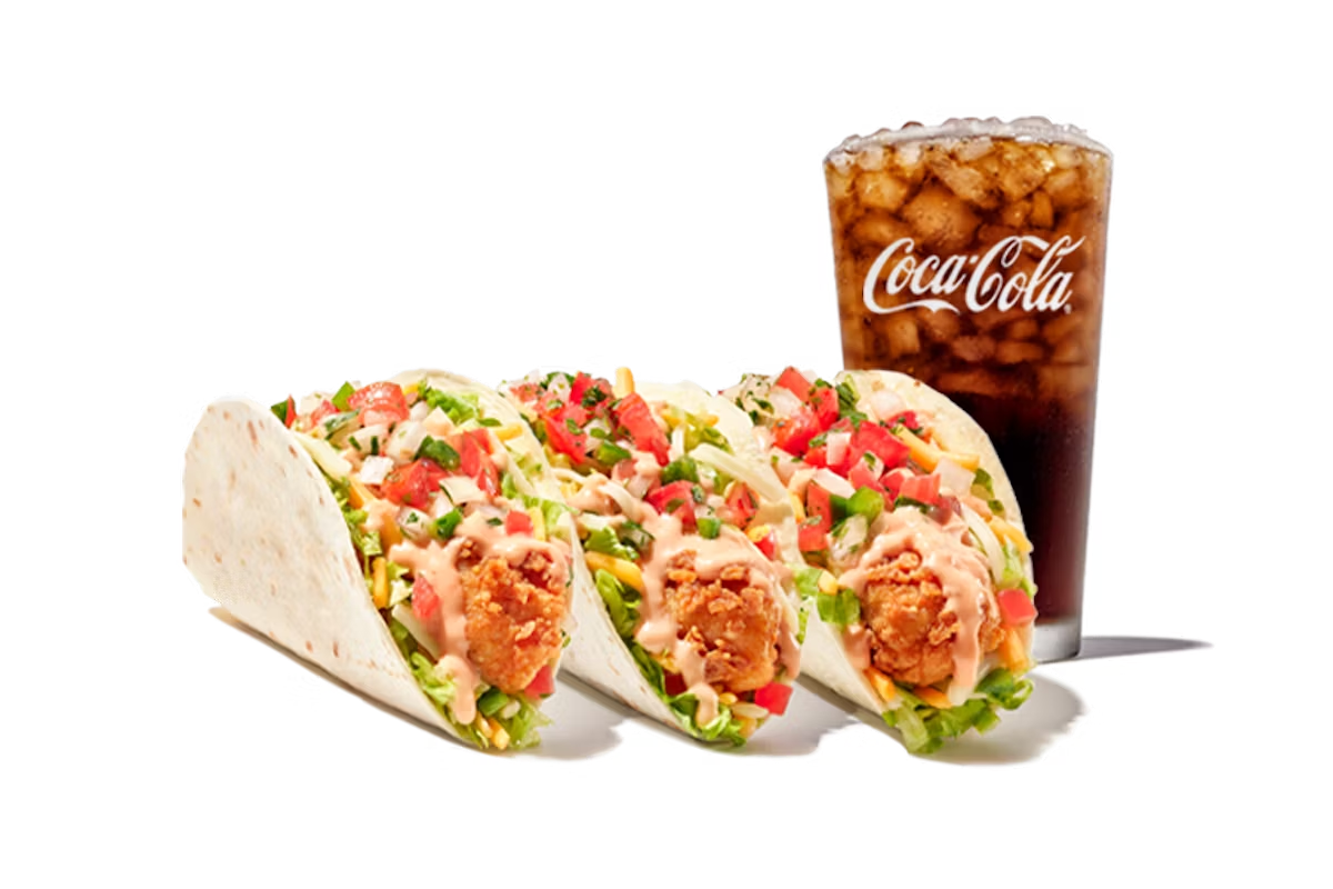 Three soft tacos from the new fast-food menu, filled with fried chicken, lettuce, diced tomatoes, shredded cheese, and creamy sauce, served with a large glass of Coca-Cola filled with ice—all on a white background.