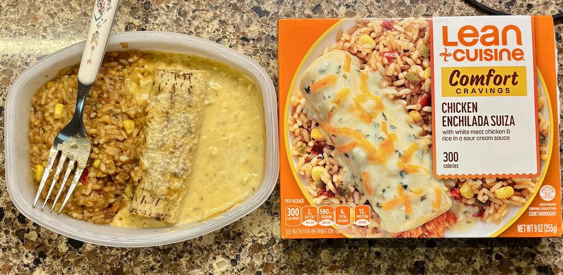 A Lean Cuisine Comfort Cravings Chicken Enchilada Suiza meal is shown, with the cooked food in a plastic tray on the left and the unopened box with a photo of the meal on the right, all on a speckled countertop.