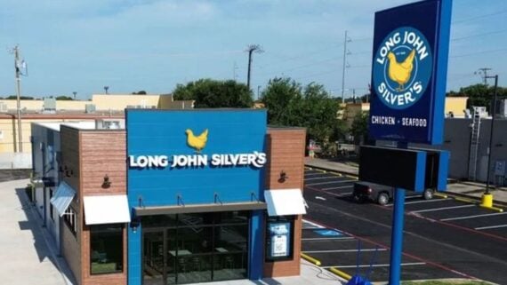 A Long John Silver’s fast food restaurant with blue signage and a yellow fish logo, seen from above. The main sign reads “Chicken • Seafood.” The parking lot and surrounding buildings are visible.
