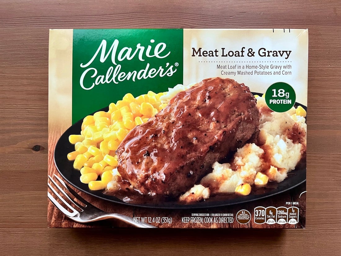 A Marie Callender’s frozen meal box featuring meat loaf with gravy, mashed potatoes, and corn on a black plate. The packaging highlights 18g protein and 370 calories, with the brand logo at the top.