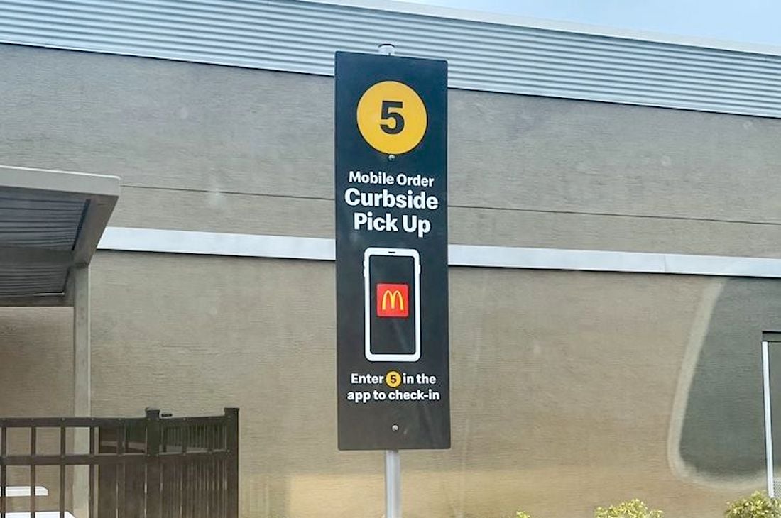 A McDonald’s curbside pick-up sign with the number 5, instructing customers to enter the number in the app to check in for mobile orders. The sign features the McDonald’s logo and an image of a phone.
