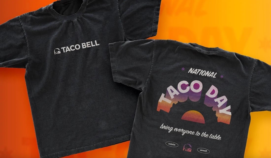 Two black T-shirts with Taco Bell branding; the front shows a small Taco Bell logo, while the back features a colorful “National Taco Day” design with a sunset graphic and the phrase “bring everyone to the table.”